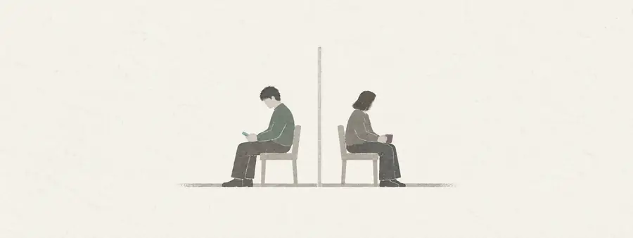 To mennesker sidder hver på sin stol med ryggen til hinanden og en tynd væg imellem sig. Den ene ser på sin telefon, den anden holder en kop.